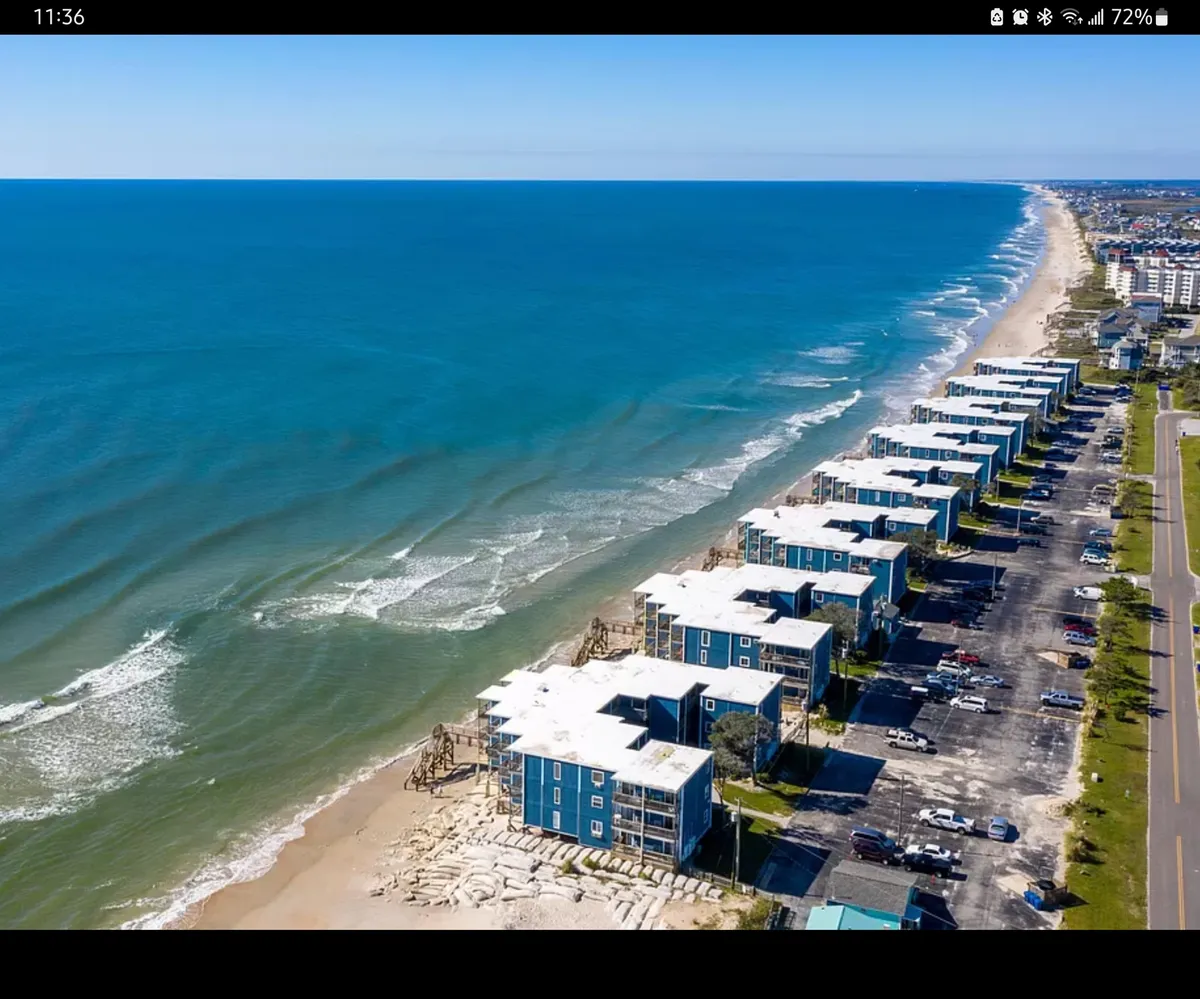 This image depicts a serene beachfront property with sweeping ocean views and nearby coastal buildings. The sun creates a tranquil atmosphere, ideal for early mornings or relaxing evenings on the balcony. The vantage point suggests close proximity to both the beach and neighboring amenities.