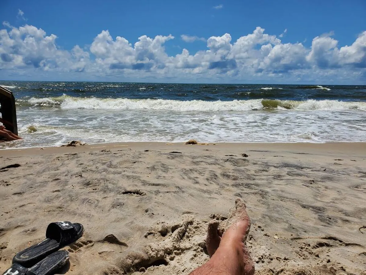 Close-up view of a sun-kissed sandy beach with gentle ocean waves and a foot stepping into the sand. The atmosphere is calm and inviting, highlighting the ease of reaching the beach and the soothing natural environment just outside the condo.